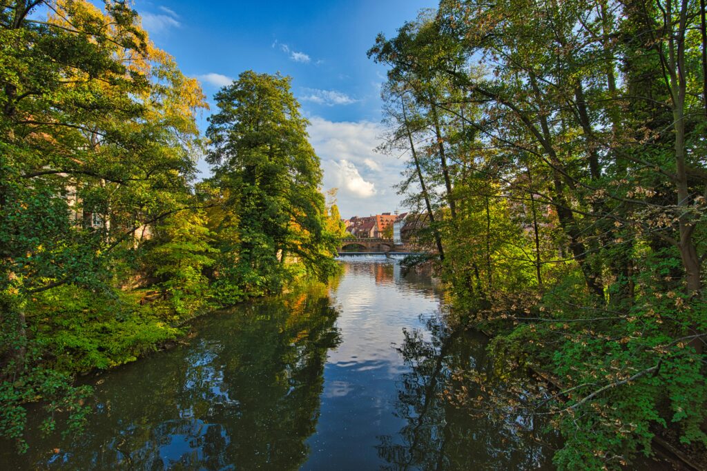 Peaceful river scene in Nuremberg, Germany with lush green trees reflecting in the water.